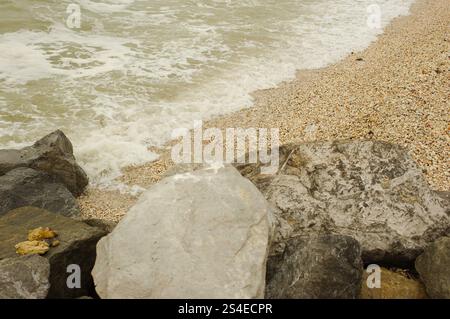 Vista ravvicinata di Diagonal sulle grandi rocce di St. Pete Beach, Florida, con sabbia e acqua spumeggiante. Onde bianche che si tuffano su grandi rocce Foto Stock