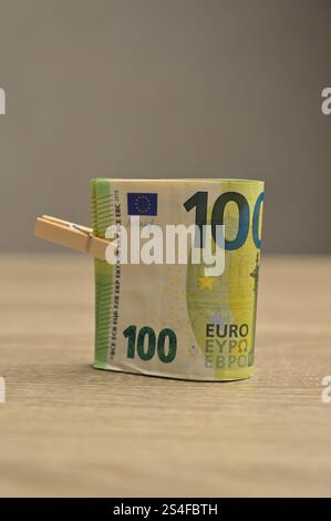 Rotolo di banconote da 100 euro in contanti con una piccola clothespin su un fondo di legno, isolato Foto Stock