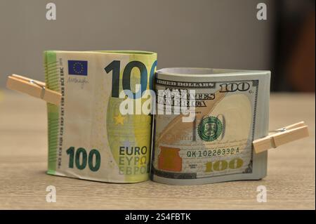 Rotoli da 100 banconote americane e da 100 euro in carta con un piccolo clothespin su un fondo di legno Foto Stock