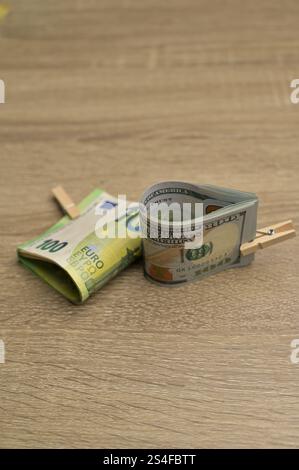 Rotoli da 100 banconote americane e da 100 euro in carta con un piccolo clothespin su un fondo di legno Foto Stock