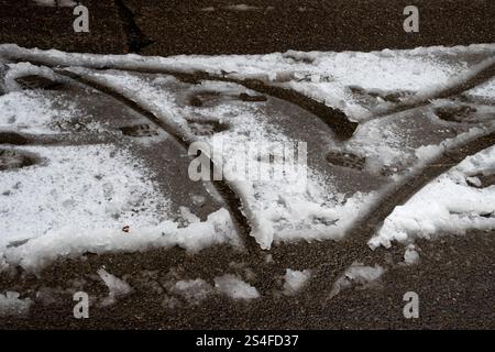 Un'immagine che mostra le tracce e le impronte degli pneumatici incorporati nella neve che scioglie su una pavimentazione bagnata, simboleggiando l'impatto dell'inverno sull'ambiente e sugli elementi di Foto Stock