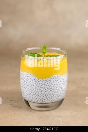 Budino di semi di chia, latte di cocco, purea di mango in una tazza di vetro, macro. Su sfondo beige. Dessert crudi, vegani e senza zucchero Foto Stock