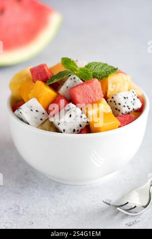 Macedonia di frutta con mango, anguria, frutto del drago, ananas, menta e forchetta su sfondo grigio. Macedonia di frutta tailandese. Foto Stock