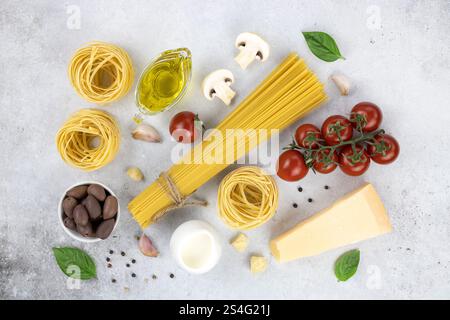 Ingredienti per cucinare pasta, spaghetti, tagliatelle, olive, pomodori, formaggio, olive su sfondo grigio. Foto Stock