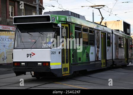 Tram di classe B, con livrea bianca e verde con logo PTV sul davanti, che attraversa un incrocio nella periferia di Melbourne in serata Foto Stock