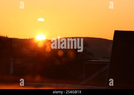 Una fotografia di un'alba su abitazioni e colline di periferia. Sagome mattutine con antenne tv, cavi, tetti e montagne Foto Stock