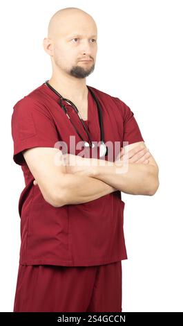 Un medico maschio calvo con la barba, con scrub rossi e uno stetoscopio intorno al collo, sta con le braccia incrociate. Foto Stock