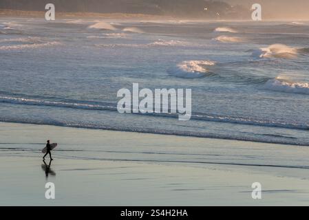Surfista che cammina a Kiwanda Beach, Oregon. Foto Stock