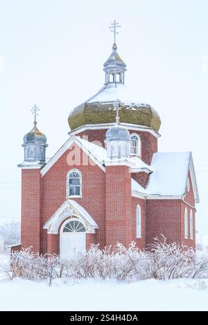 Una piccola chiesa in mattoni con un campanile e una croce in cima. L'edificio è coperto di neve Foto Stock