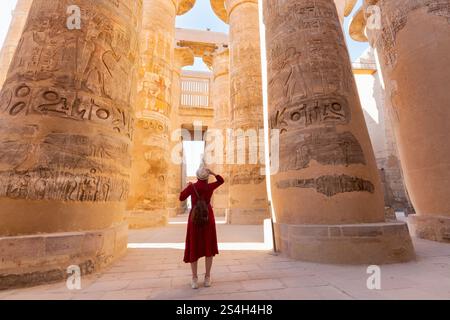 Donna viaggiatore esplora le rovine dell'antico tempio di Karnak nella città di Luxor in Egitto. Grande fila di colonne con geroglifo scolpito Foto Stock
