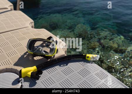 Vicino all'acqua turchese, c'è un molo di plastica dove si trovano una maschera gialla e un boccaglio. Foto ad alta risoluzione. Foto Stock