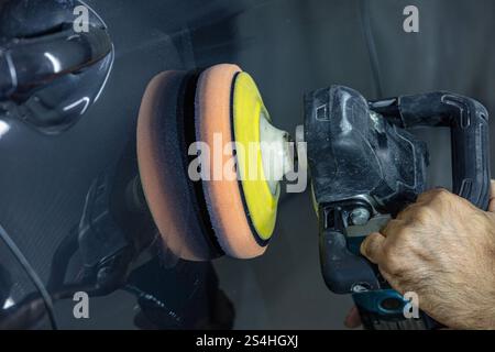 Auto cera polacco lavoratore mani applicando il nastro protettivo prima della lucidatura. Pulitura e lucidatura auto. Dettagli auto. Chi detiene un lucidante in mano e Foto Stock
