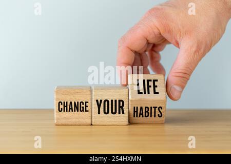 La mano gira il blocco di legno e cambia le parole cambia le tue abitudini in slogan cambia la tua vita. Foto Stock
