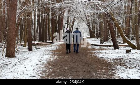 Coppia matura che va su un sentiero innevato nella pineta invernale. Marito anziano e moglie camminano attraverso il sentiero nel bosco di conifere. Coppia più vecchia di Foto Stock