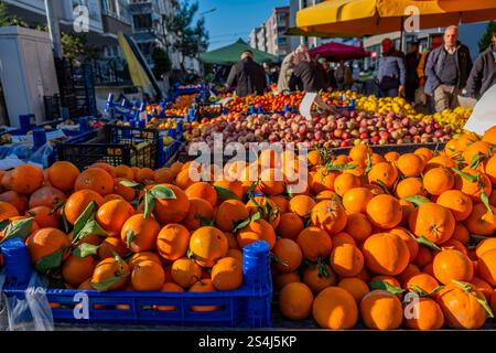 Un grande mucchio di arance viene esposto in un mercato. Le arance sono accumulate in casse e cesti, e ci sono diverse persone che camminano intorno al ma Foto Stock