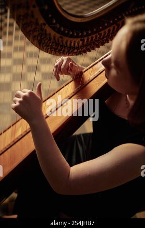 Ripresa ad alto angolo di una musicista femminile irriconoscibile che suona un'incantevole melodia su un'arpa che succhia delicatamente le corde mentre esegue musica nella philharmonic Hall Foto Stock