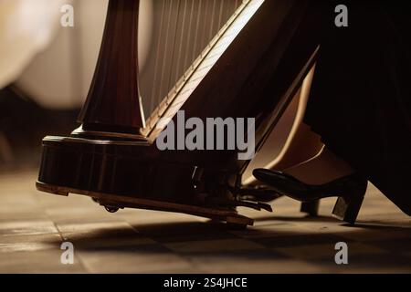 Primo piano su tonalità calde di musicisti femminili piede in scarpe classiche nere premendo il pedale dell'arpa che esegue musica classica al chiuso, spazio copia Foto Stock