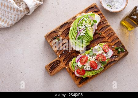 Due brindisi all'avocado guarniti con pomodori, ravanelli e formaggio feta presentati elegantemente Foto Stock