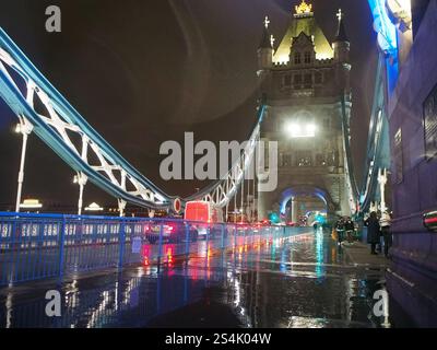 Auto e pedoni sotto la pioggia sul Tower Bridge di notte a Londra, Regno Unito a febbraio. Visto arrivare dalla Torre di Londra. Foto Stock