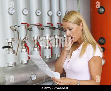 Una giovane donna con una bolletta per il riscaldamento. Nella sala caldaie, Austria, Europa Foto Stock