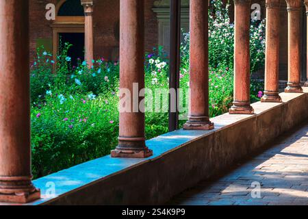 Colonne del chiostro illuminate dal sole che incorniciano un sereno giardino con fiori, che offre un tranquillo mix di eleganza architettonica e bellezza naturale. Ideale per i temi Foto Stock