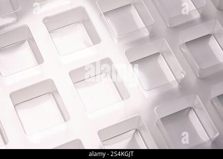 Uno stampo per termoformatura quadrato trasparente industriale realizzato in plastica come soluzione di imballaggio per prodotti industriali. Vassoio in lamina su sfondo grigio. Foto Stock
