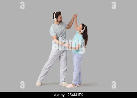 Coppia innamorata in pigiama con cuffie che ballano su sfondo chiaro Foto Stock