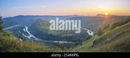 Una vista mozzafiato pittoresca di un fiume che scorre attraverso una lussureggiante valle verde durante l'alba Foto Stock