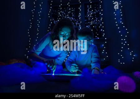 Bambino e terapista in camera stimolante sensoriale, Black snoezelen. Bambino autistico che gioca con il terapista durante la sessione di terapia occupazionale. Foto Stock