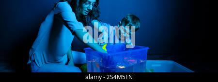 Bambino e terapista in camera stimolante sensoriale, Black snoezelen. Bambino autistico che gioca con il terapista durante la sessione di terapia occupazionale. Foto Stock