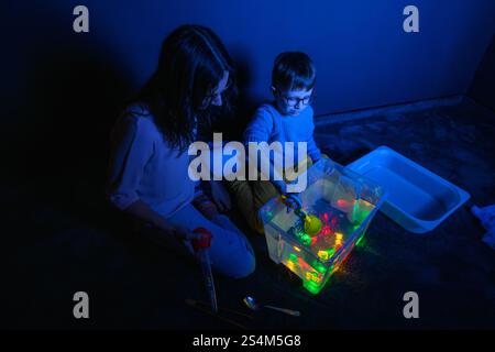 Bambino e terapista in camera stimolante sensoriale, Black snoezelen. Bambino autistico che gioca con il terapista durante la sessione di terapia occupazionale. Foto Stock