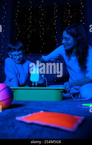 Bambino e terapista in camera stimolante sensoriale, Black snoezelen. Bambino autistico che gioca con il terapista durante la sessione di terapia occupazionale. Foto Stock