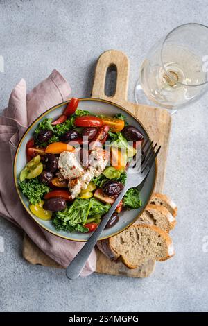 Vista dall'alto di un'insalata sana con foglie di cavolo crude, pomodori ciliegini in vari colori, fette di cipolla rossa, olive e formaggio feta speziato. Aziende Foto Stock