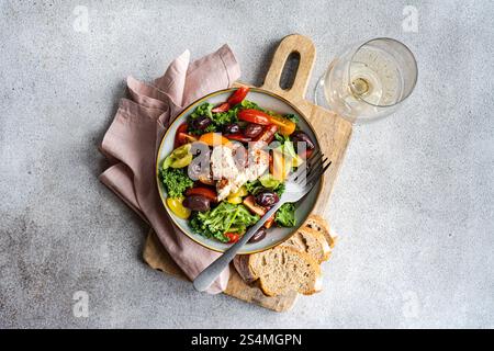 Vista dall'alto di un'insalata con cavolo crudo, pomodori ciliegini assortiti, fette di cipolla rossa, olive aromatizzate al barbecue e formaggio feta speziato, sapientemente condito Foto Stock