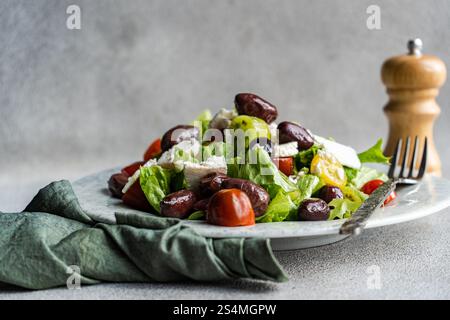 Una vivace insalata greca con pomodori, lattuga e olive rosse, condita con formaggio feta e olio d'oliva accompagnati da uno shaker di pepe Foto Stock