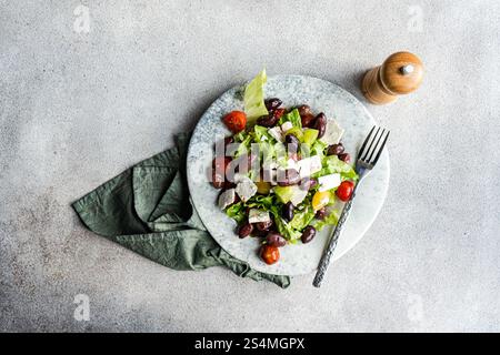 Una vivace insalata greca con pomodori, lattuga, olive rosse, olio d'oliva e formaggio feta accompagnati da uno shaker di pepe Foto Stock