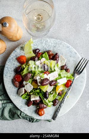 Una vivace insalata greca con pomodori freschi, lattuga croccante, olive rosse fermentate e formaggio feta cremoso, abbinato a un bicchiere di vino bianco ghiacciato Foto Stock