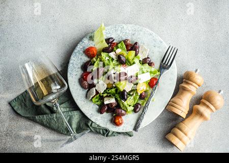 Una vivace insalata greca con pomodori succosi, lattuga croccante, feta e olive rosse, abbinata a un bicchiere di vino bianco freddo su un tavolo rustico Foto Stock
