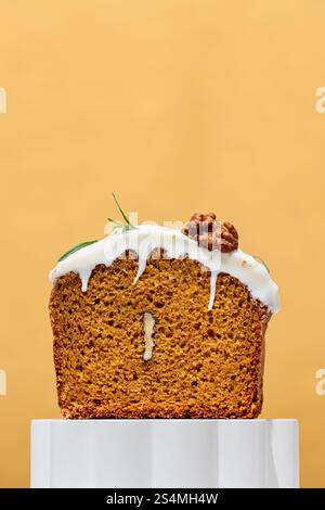 Un appetitoso pane di carote con cremosa glassa bianca si trova su un caldo sfondo arancione ricoperto di noci e rosmarino, questo dessert è un vero e proprio Foto Stock
