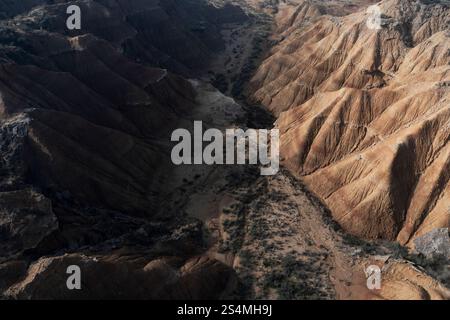 Vista aerea di un aspro canyon nel deserto con scogliere ripide ed erose e un letto asciutto del fiume le Ombre sottolineano la drammatica struttura e le formazioni naturali del Th Foto Stock