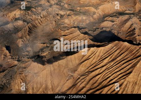 Vista aerea che raffigura un aspro terreno desertico caratterizzato da imponenti creste e calanchi la luce del sole getta ombre, evidenziando gli intricati schemi di erosi Foto Stock