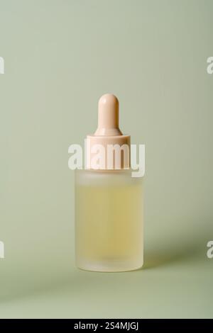 Un'elegante bottiglia per siero in vetro smerigliato con contagocce, riempita con un liquido giallo pallido, si staglia su uno sfondo verde pastello, a indicare una serena e Foto Stock