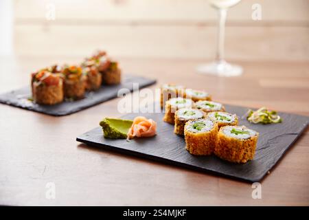 Un'elegante disposizione di sushi roll su un'ardesia nera, con rotoli croccanti e hosomaki, completati da wasabi e zenzero sottaceto. L'impostazione i Foto Stock