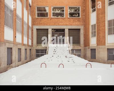 Una tranquilla scena cittadina caratterizzata da una scala innevata fiancheggiata da edifici in mattoni rossi dopo una nevicata invernale, che mostra la vita urbana in inverno. Foto Stock
