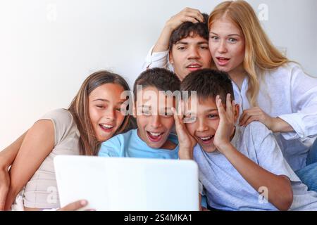 Cinque fratelli, tra cui una ragazza e due ragazzi trigemellini, si divertono con il fratello maggiore e la sorella, tutti impegnati con un notebook a casa. Foto Stock