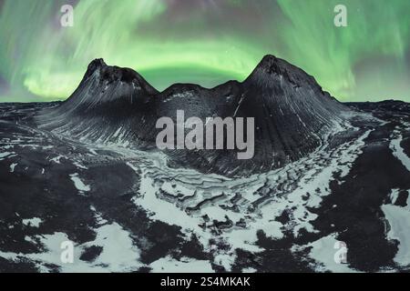 La maestosa aurora boreale balla nel cielo notturno sopra le montagne innevate e il terreno accidentato nella natura selvaggia dell'Islanda. Foto Stock
