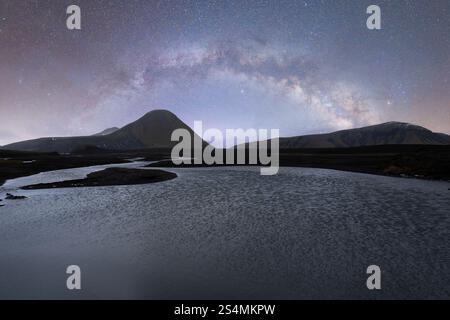 Una vista mozzafiato della via Lattea che si estende su un tranquillo paesaggio islandese, il cielo limpido e stellato illumina il tranquillo fiume e le aspre montagne Foto Stock