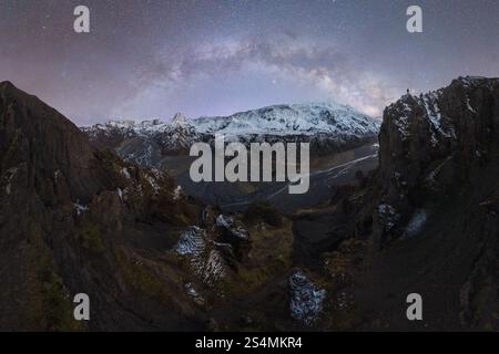 La vista delle vette islandesi sotto una notte stellata, con la via Lattea che si arrocca sul paesaggio innevato il terreno robusto e le strutture fluviali si aggiungono alla scena Foto Stock