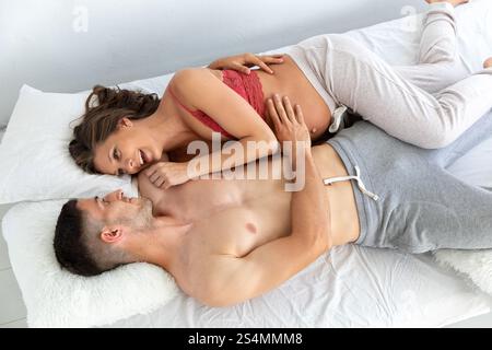 Una coppia amorevole gode di un momento di tenerezza mentre si sdraia su un comodo letto, la madre in attesa, visibilmente incinta, condivide un'espressione gioiosa con il suo partner Foto Stock