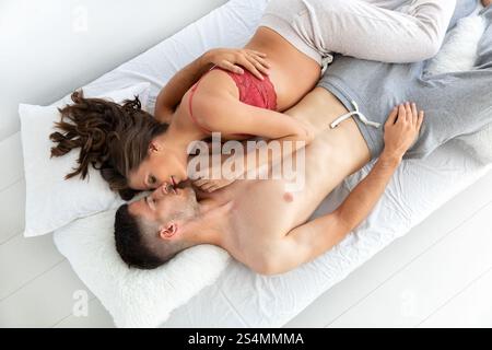 Una coppia amorevole giace su un comodo letto, con la donna incinta in un tetto rosso che abbraccia il suo partner l'atmosfera serena mette in risalto l'intimità, la conne Foto Stock